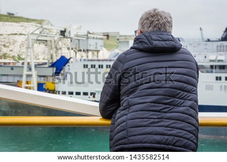 Dover, England, 15/05/2019 Man looking over the bannister of a P&O ferry at the coast of dover with a coat grey hair old glasses and beard vaping on a ship boat with coat on cold weather  Foto stock © 