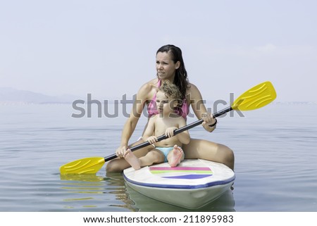 mother and son sitting on a paddle board holding a paddle over a calm sea looking to the infinite