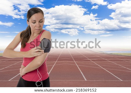 young female runner ready to run with earphones on and playing music from the mobile phone in a bangle on a running track background