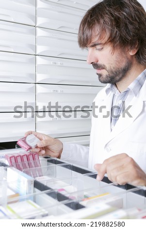 portrait of a young male pharmacist looking for a box of medicaments from a drawer - focus on the face