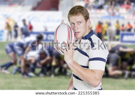 portrait of a young male rugby player standing holding a rugby ball in his hand on a background of a move by rugby