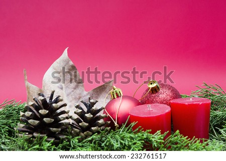 Christmas composition consisting of two red candles, two shiny red balls, pinecones and dry leaves on fir branches on a red background - focus on the red balls