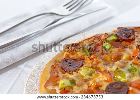closeup of a delicious homemade pizza of pepperoni and vegetables in a stone dish with a knife, a fork and a napkin beside