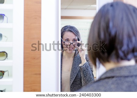 mirror image of a smiling young woman trying on glasses in optical shop - focus on the woman left eye