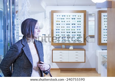 smiling young woman is entering into an optical shop with the intent to buy glasses - focus on the girl