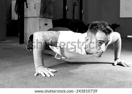 young male athlete is making push-ups at the gym, lower position - focus on the man