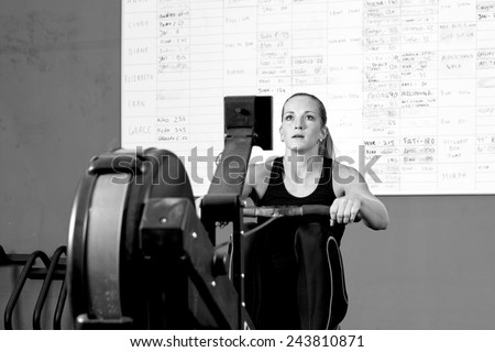 concentrated female athlete is exercising on rowing machine in the gym - focus on the woman
