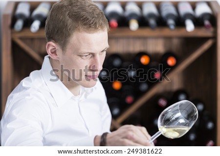 young man on a wine tasting session on the visual phase examining a white wine on a placemat at a restaurant - focus on the man face