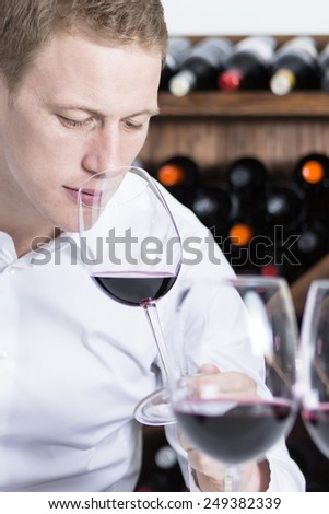 closeup of a young man on a wine tasting session on the olfactory phase with the wineglass in the nose is writing down in a wine tasting sheet at a restaurant - focus on the man face