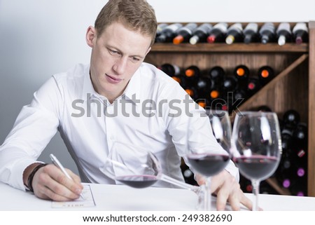young man on a wine tasting session on the visual phase is writing down in a wine tasting sheet at a restaurant  - focus on the man face