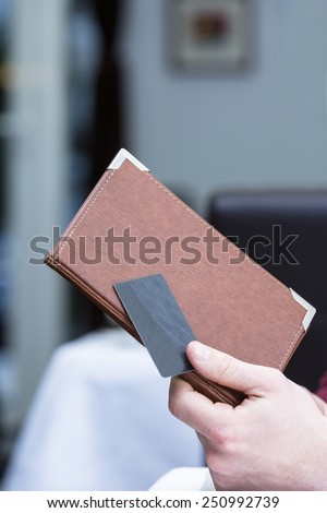 closeup of the hand of a businessman holding a bill cover and a credit card at the end of a working lunch at a restaurant - focus on th thumb