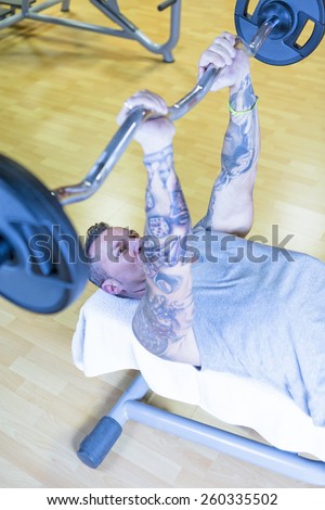 man making french press - triceps exercise - lying on a bench at the gym - start exercise - focus on the man face