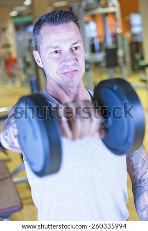 closeup of a man making standing dumbbell front raises - shoulder exercise - at the gym - finish exercise - focus on the man face