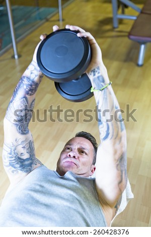 young man making dumbbell pull overs - chest exercise - lying on a bench at the gym - finish exercise - focus on the man face