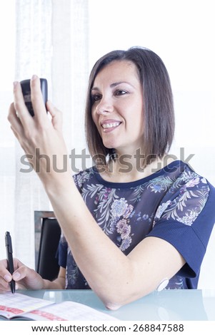 smiling young woman is looking at a reader after scanning the sensor of the glucose monitoring system ready to write the value on a blood glucose diary at home - focus on the woman right eye