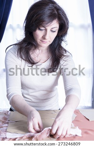 dressmaker is sewing the fabric of a fashion design on her work table at her sewing atelier - focus on the face