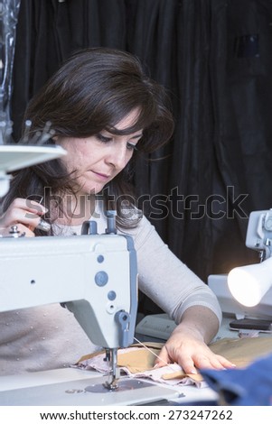 seamstress is sewing the pattern to the fabric seated on a sewing machine at her sewing atelier - focus on her right eye