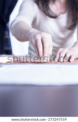 close up of the hands of a seamstress marking a fabric with a chalk at her sewing atelier - focus on the chalk