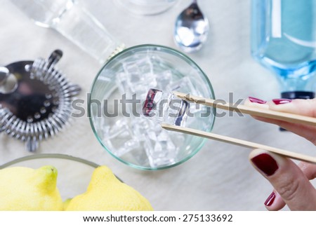 closeup of a woman hand taking ice cubes from an ice bucket with a bamboo ice tongs on a gin tonic session - focus on the ice cube