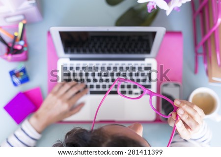 top view of a woman putting on glasses on a working desk - focus on the glasses