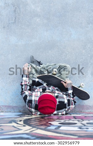 top view of an old man skater sitting on the floor with a skateboard at a skate park - focus on the forehead