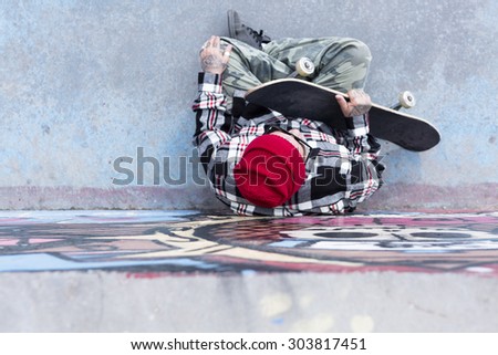 top view of an old man skater sitting on the floor with his skateboard at a skate park - focus on the head