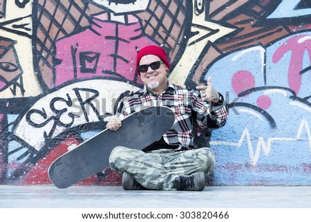 portrait of an smiling old man skater sitting on the floor with his skateboard at a skate park - focus on the face