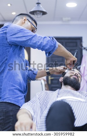 hairstylist on a beard shaving session and a customer on a barber chair on the barber shop - focus on the barber face