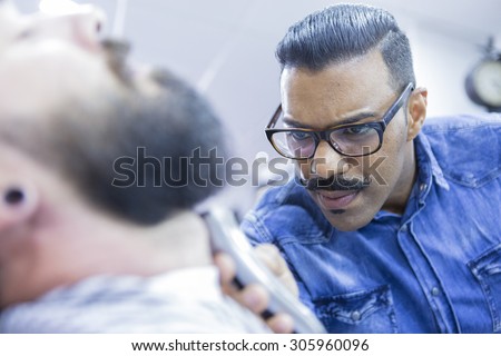 young barber shaving a beard of a customer in a barber shop - focus on the left eye