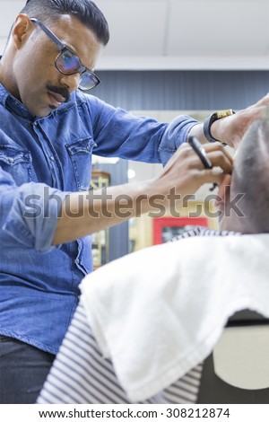 concentrated hairstylist is shaving a beard of a customer in a barber shop - focus on the face