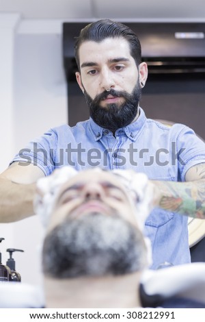hairstylist is massaging hair of a customer sitting on the shampoo chairs on his barber shop - focus on the hairstylist left eye