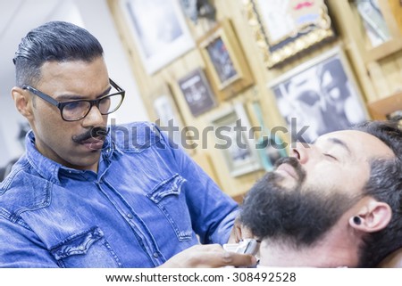 young barber is shaving a beard of a customer in a barber shop - focus between the barber eyes