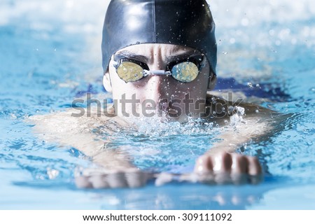 closeup of a male swimmer swimming with a swim board doing leg exercises in an indoor swimming pool - focus on the face