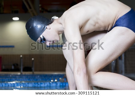 male swimmer on the edge of an indoor swimming pool ready to jump - focus on the goggles