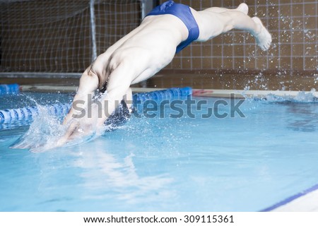male swimmer is diving head first from the edge of an indoor swimming pool  - focus on the right arm