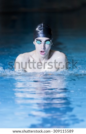male swimmer is breathing on a breaststroke exercise in an indoor swimming pool  - focus on the face