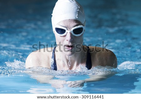 female swimmer is breathing on a breaststroke exercise in an indoor swimming pool  - focus on the face