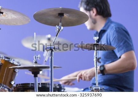 detail of a cymbal with an unfocused drummer playing drums on background in a recording studio - focus on the cymbal stand