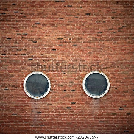 Two round windows on a brick wall facade, looking like eyes