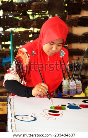 TERENGGANU, MALAYSIA - APRIL 16,2014 - An artist carefully trace on a traditional batik at Noor Arfa Craft Complex, Terengganu, Malaysia