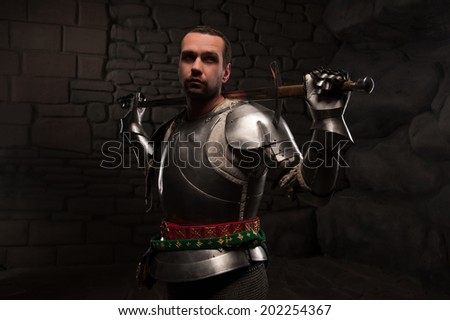 Medieval Knight posing with sword in a dark stone background. Waist up portrait.