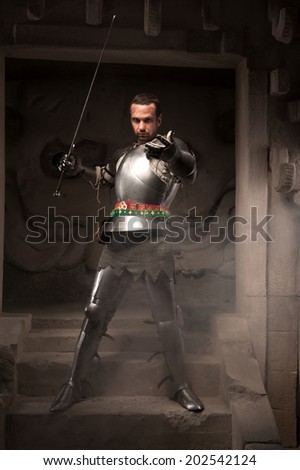 Young masculine man in historical costume. Medieval warrior with armor and sword reaching out on steps of ancient temple, dark