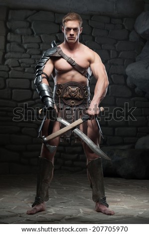 Full length portrait of young attractive warrior gladiator with muscular body posing with two swords on dark background. Concept of masculine power, strength