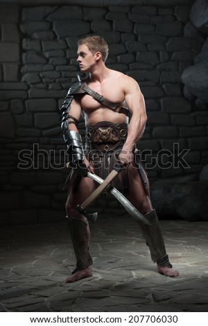 Full length portrait of young attractive warrior gladiator with muscular body posing with two swords, looking aside on dark background. Concept of masculine power, strength