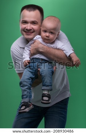 Portrait of happy smiling handsome father and his son baby boy in white polo shirt and jeans posing, family concept, isolated on green background