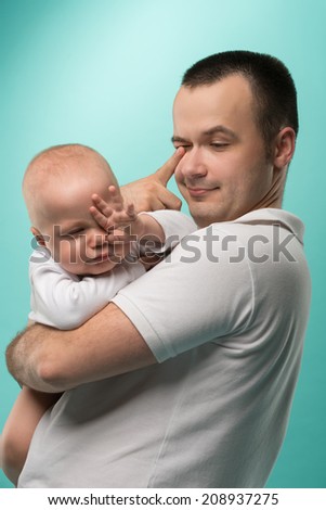 Happy handsome smiling Caucasian father holding his son baby boy preparing to sleep isolated on blue. Family concept, closeup