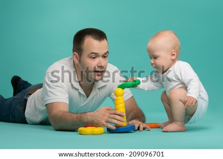 Happy handsome smiling Caucasian father playing with his son baby boy, picking up pyramid circles, isolated on blue. Family fun concept