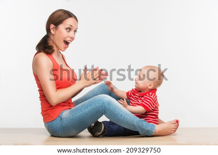 Portrait of young attractive Caucasian mother sitting face to face to her cute toddler son playing clapping hands, lifestyle fun concept, isolated on white