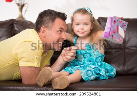 Cute little smiling girl having fun with her father sitting on the sofa, father pointing at something