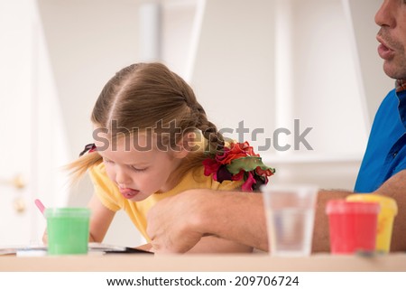 Half-length closeup portrait of little beautiful kid with pigtails, cute girl and her father painting with marker ink pen, pens and paints on the  desk, interior shot